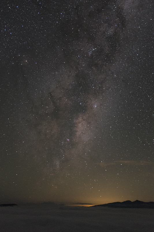 Astrophotography of the milky way above a layer of cloud with a glow in the distance