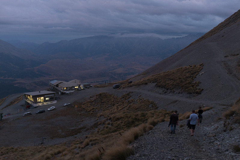 Three people at dusk gently descend a stony slope toward the inviting lights of the day lodge and night lodge